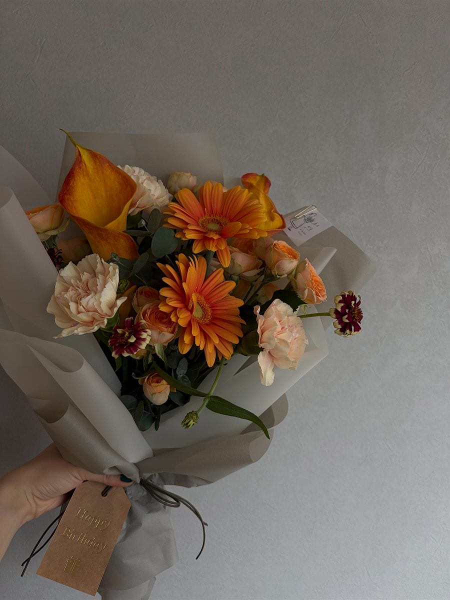 オレンジのガーベラとカラーを束ね、灰色の紙で包んだ贈りもの用の花束