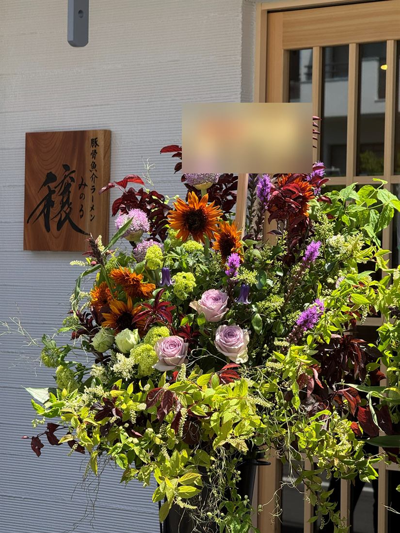 開店祝いのスタンド花。店舗の入口に、ひまわりと深紅の葉、淡い紫のバラを組んで設置されている